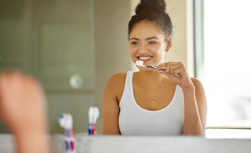 young woman brushing teeth in mirror