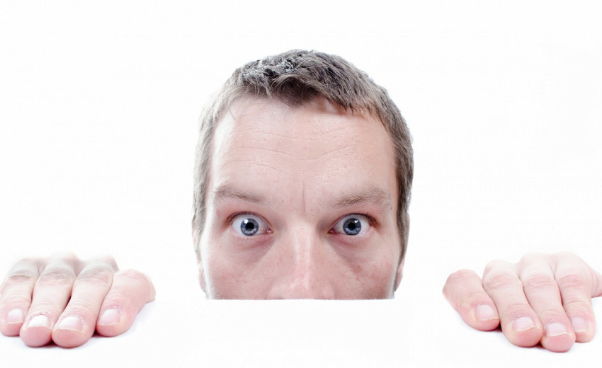 man hiding behind white counter looking scared