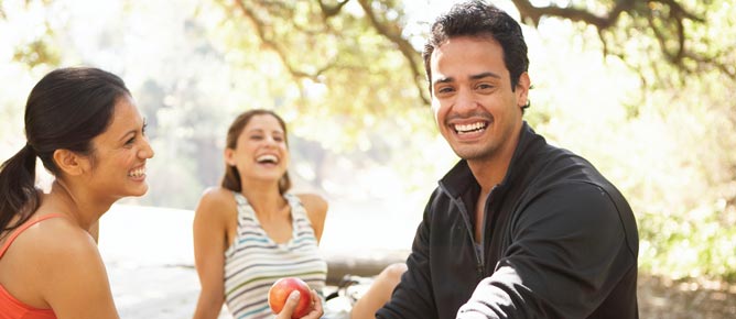 brunette woman holding apple, brunette woman laughing, and brunette man smiling