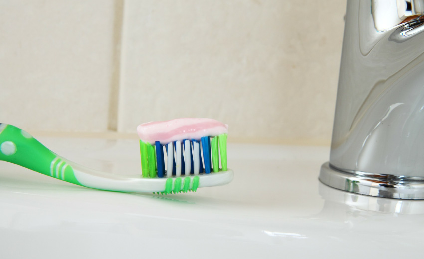 green and blue toothbrush with toothpaste, sitting on sink