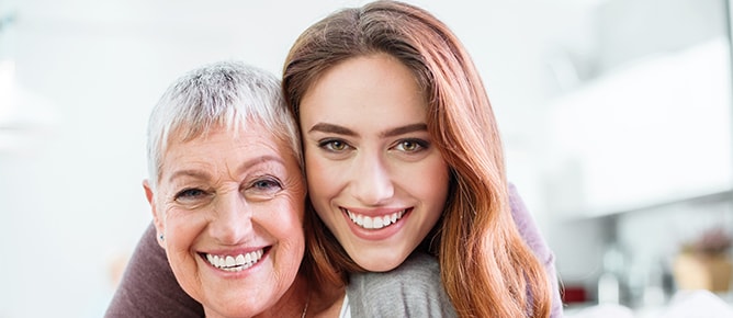 An older woman with a dental bridge smiling with her daughter.