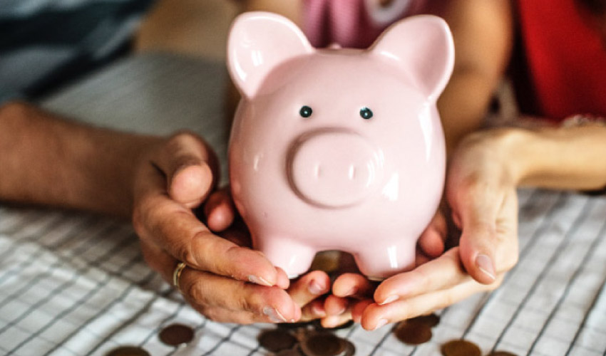 hands holding a pink piggybank spilling coins out the bottom