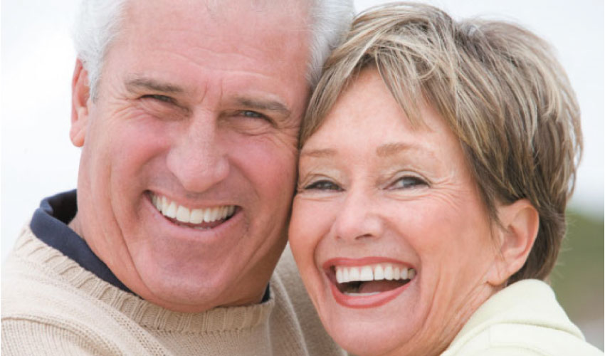 senior couple hugging and smiling after learning about the benefits of dentures