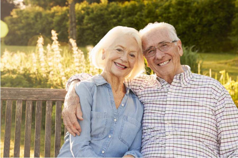 senior couple sitting on a bench hug and smile after learning about caring for their dentures