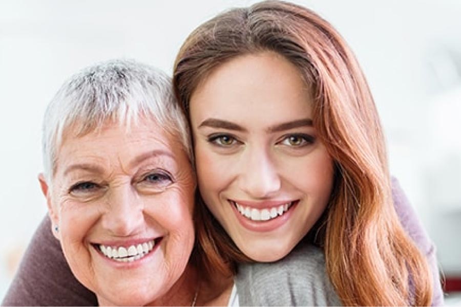 a young woman and a senior woman smile together after learning about dental bridges