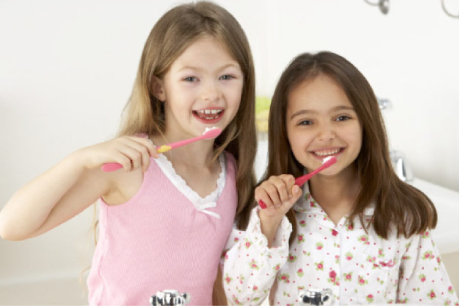 two young girls excited about oral health brush their teeth together