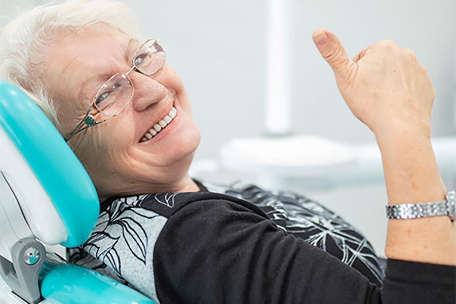 senior women in the dentist chair gives a thumbs up after learning about teeth replacement options