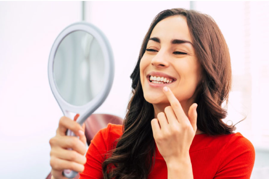 woman looks in a hand held mirror at her sensitive teeth