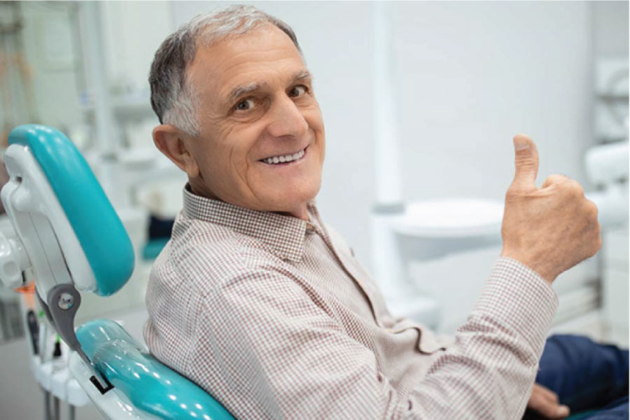 senior man sitting in the dentist chair gives a thumbs up