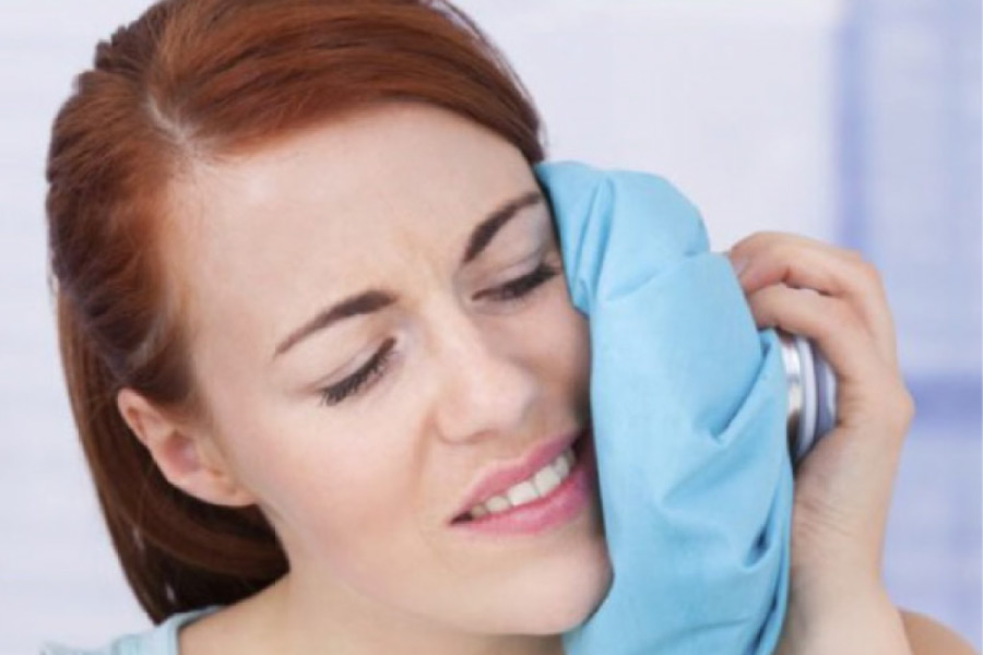 woman holds an ice pack to her cheek after tooth extraction surgery