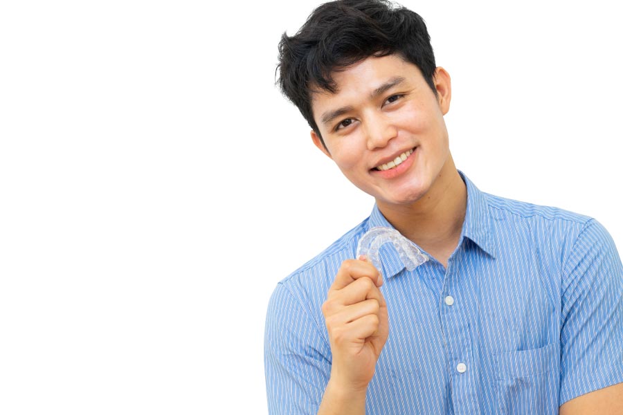 young man holds up his Invisalign clear aligner and smiles.