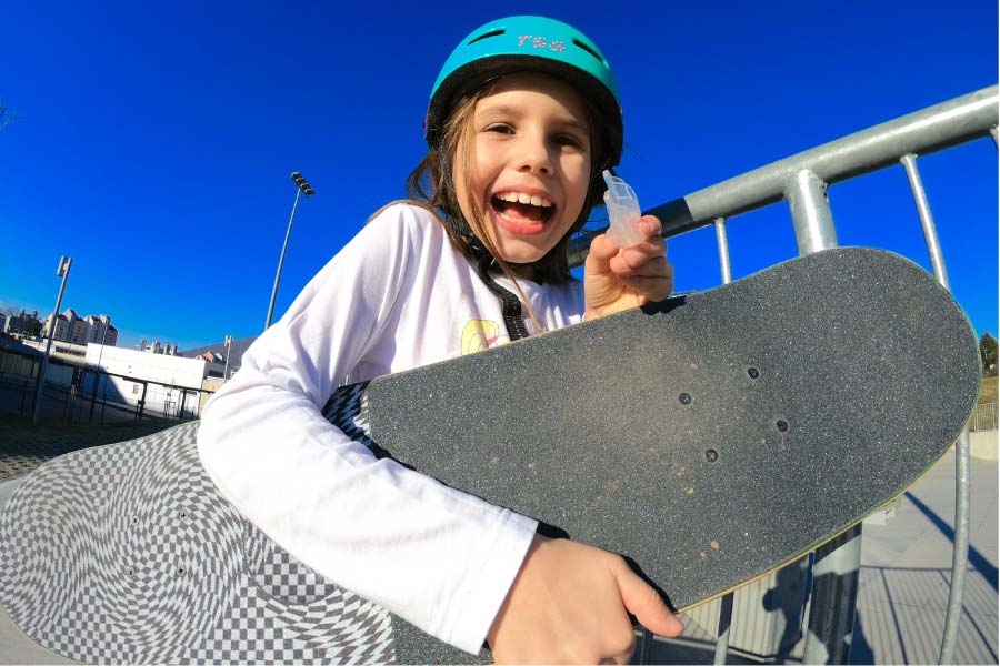 young girl wearing a helmet with a skateboard under her harm hold up her mouthguard
