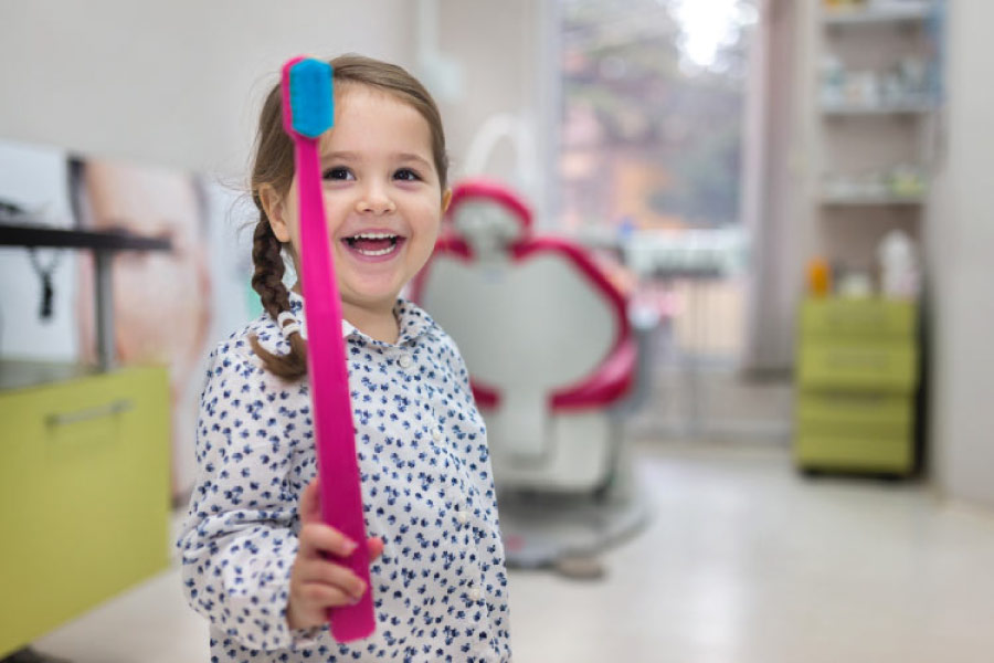 young girl holding a giant toothbrush at the dentist office