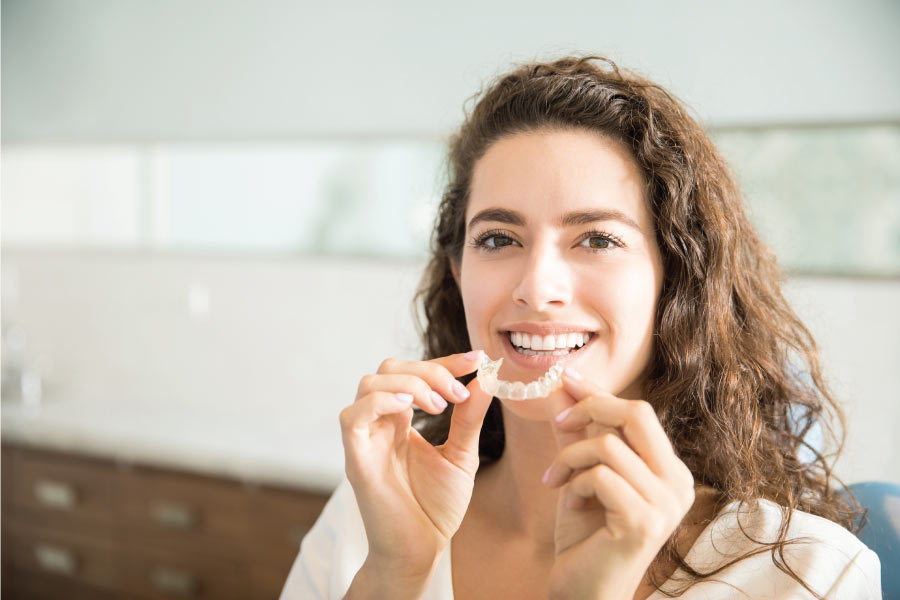 young woman smiles as she inserts her clear aligner to straighten teeth